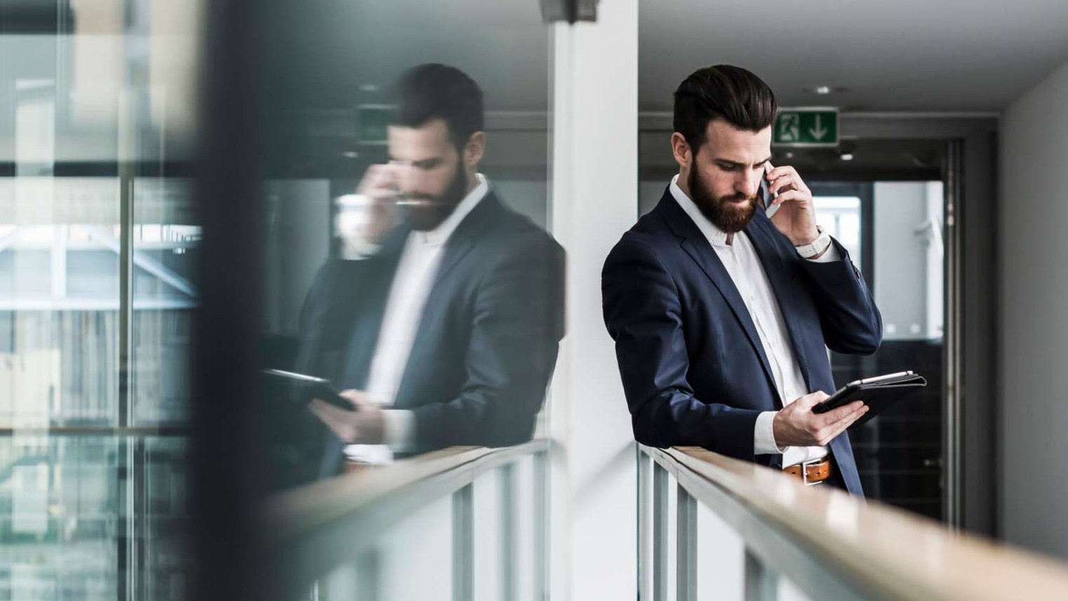 Mann mit Handy und Laptop lehnt am Geländer im Flur