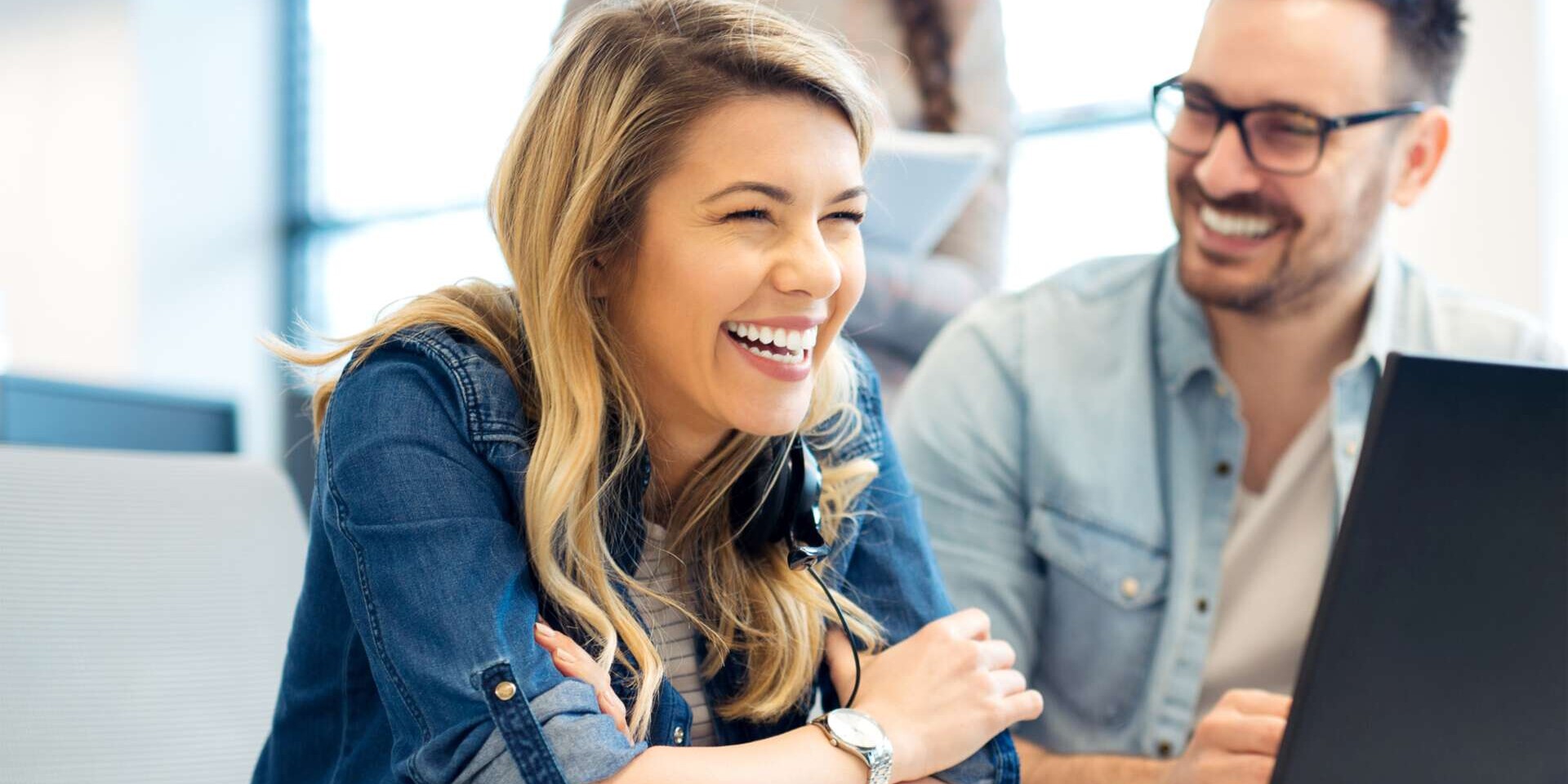 Eine Frau und ein Mann in einer Bürosituation vor einem Laptop, die Personen lachen