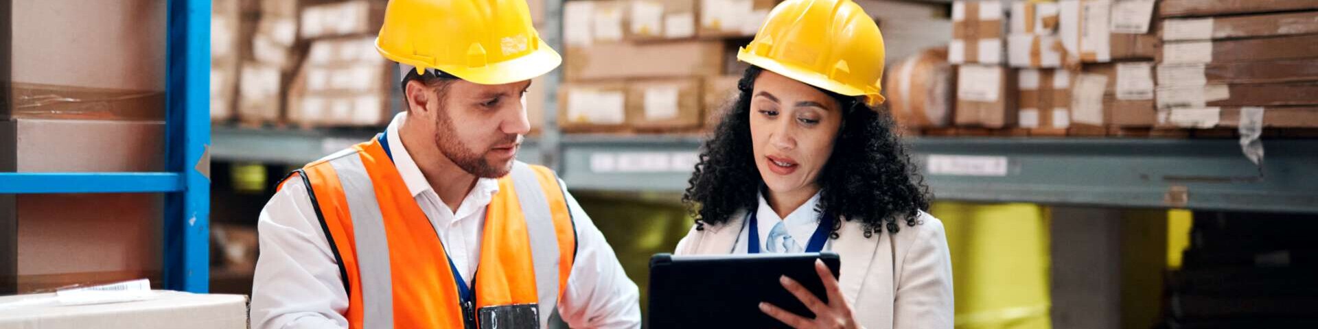 Zwei Beschäftigte stehen im Lager, die Frau zeigt ihrem Kollegen etwas auf dem Tablet. 