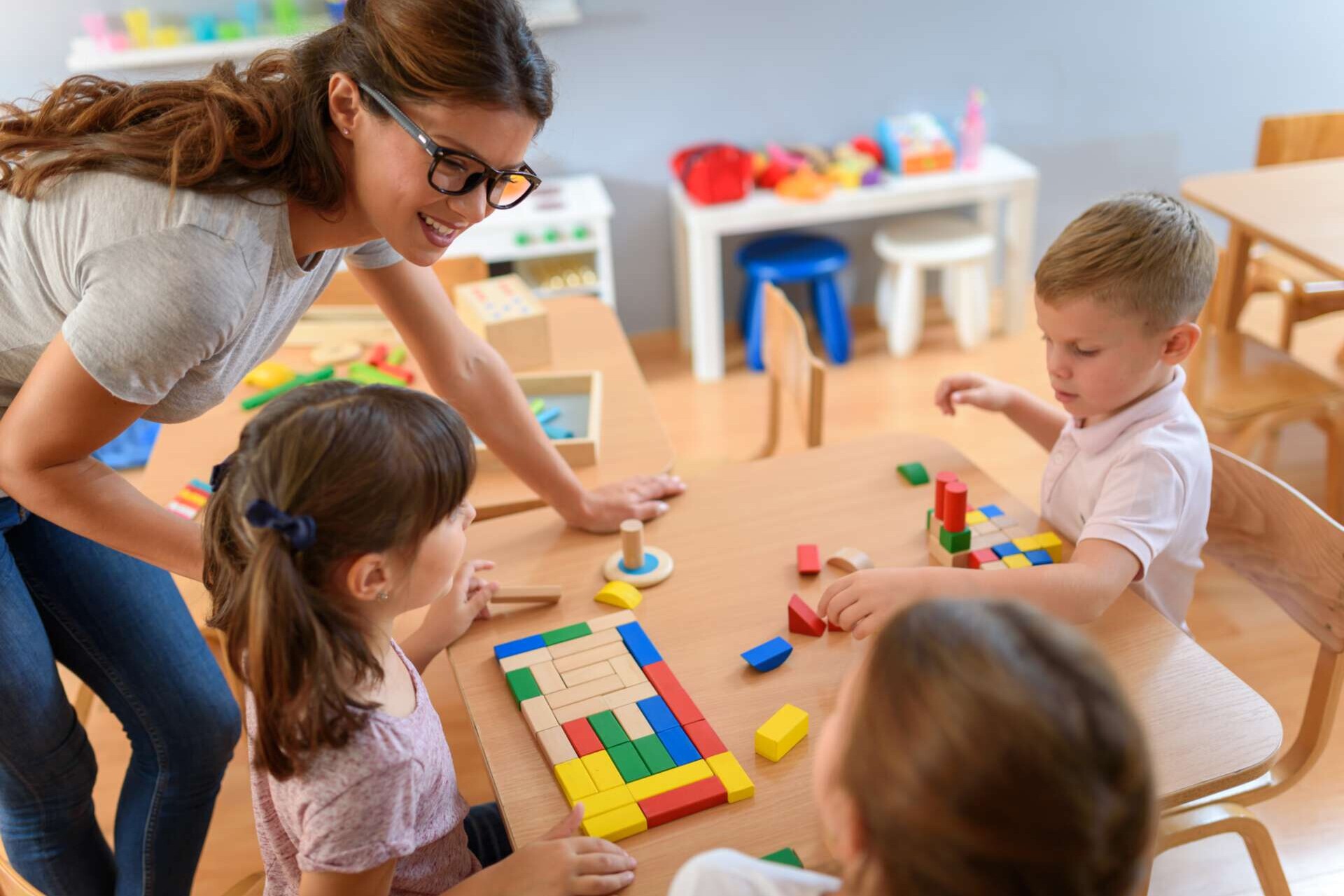 Erzieherin mit Kindern, die im Kindergarten mit bunten Holzspielzeugen spielen