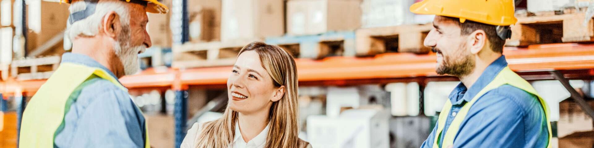 Drei Personen in einem Lager. Die Leiterin schüttelt dem älteren Mitarbeiter die Hand.