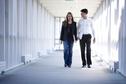 Zwei Personen laufen während einem Gespräch den Flur entlang