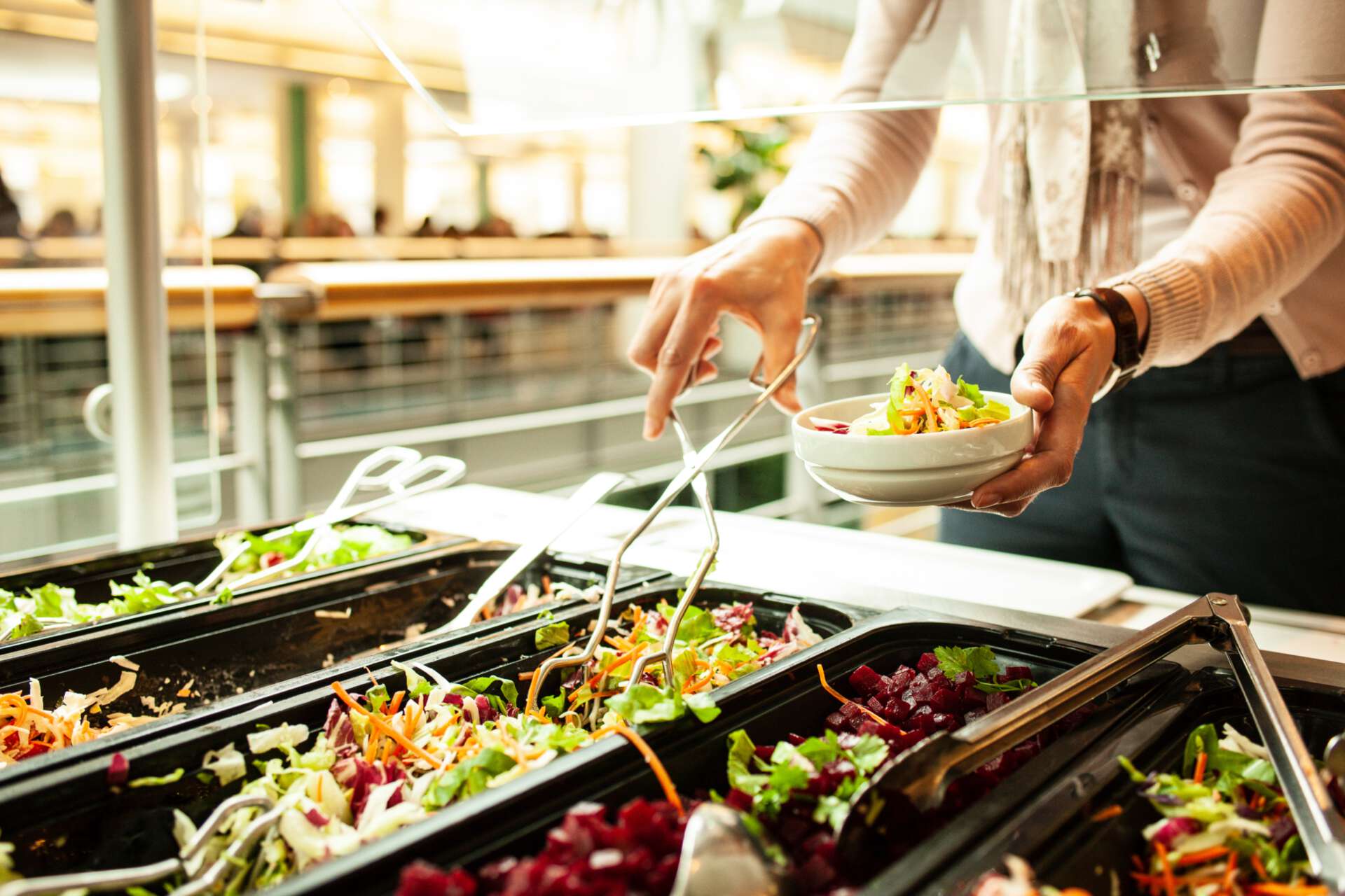 an der Salatbar stellt sich jemand mit der Zange einen eigenen Salat zusammen