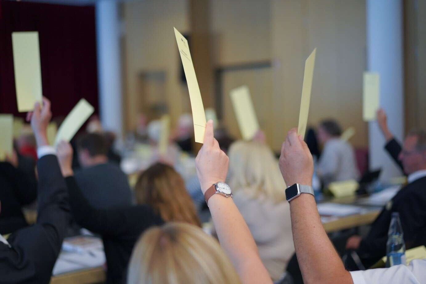 Viele Hände halten einen gelben Wahlzettel in die Luft