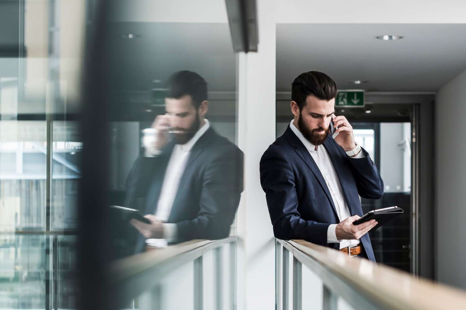 Mann mit Handy und Laptop lehnt am Geländer im Flur