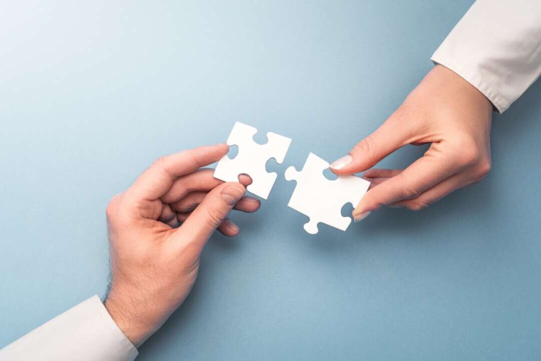 Zwei Menschen, die Puzzleteile in den Händen aneinander halten.