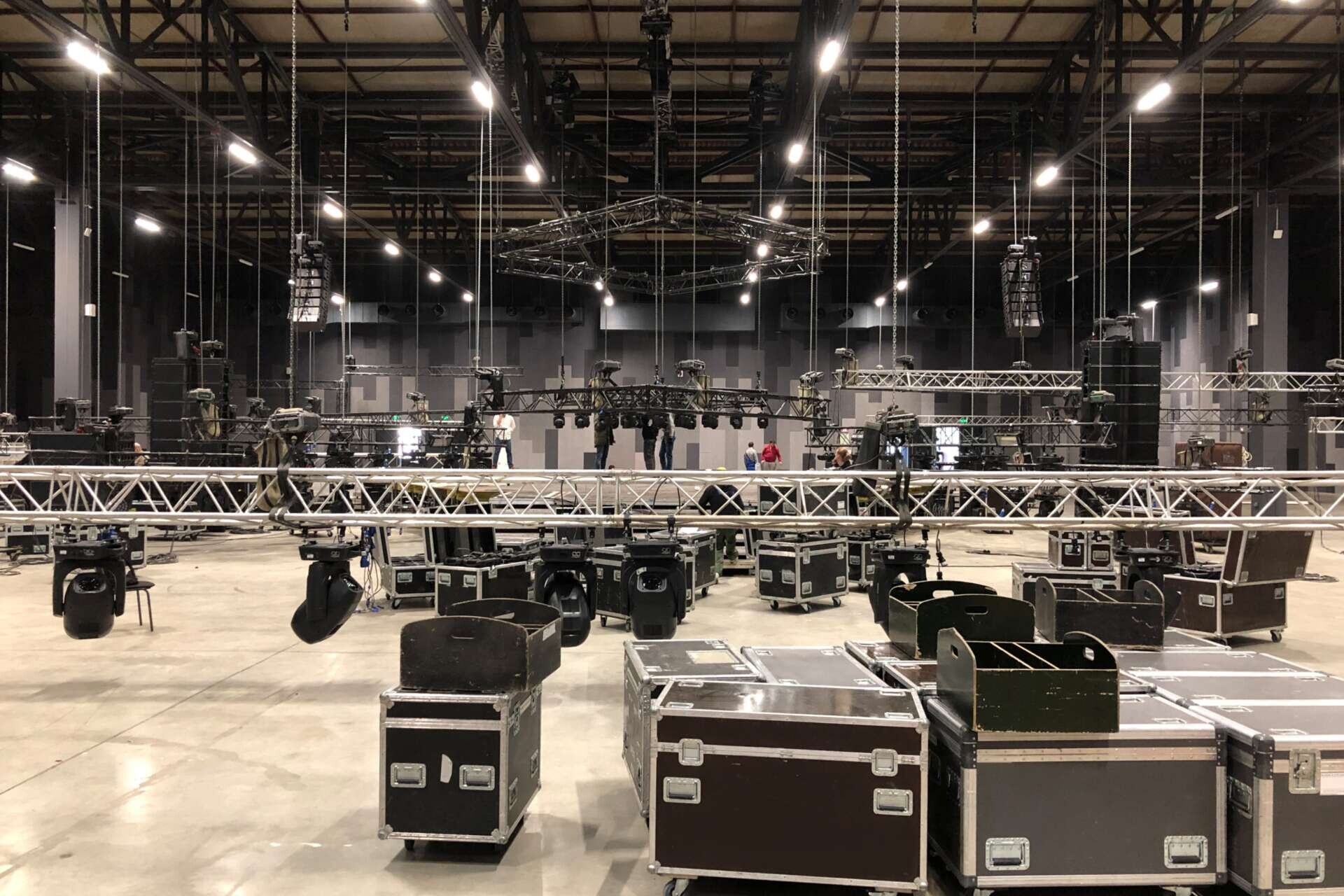 Installation professioneller Ton-, Licht-, Video- und Bühnentechnik für ein Konzert. Bühnenbeleuchtungsgeräte werden zum Heben auf eine Traverse geklemmt. Flightcases mit Kabeln.#RLNCH_XXIII