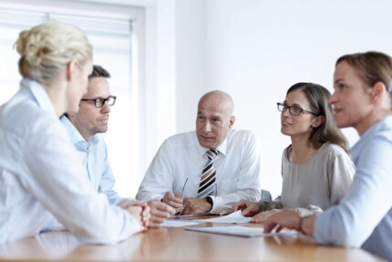 drei Frauen und zwei Männer sitzen am Besprechungstisch